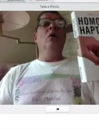 Ein Mann mit Brille hält ein Buch in die Kamera.